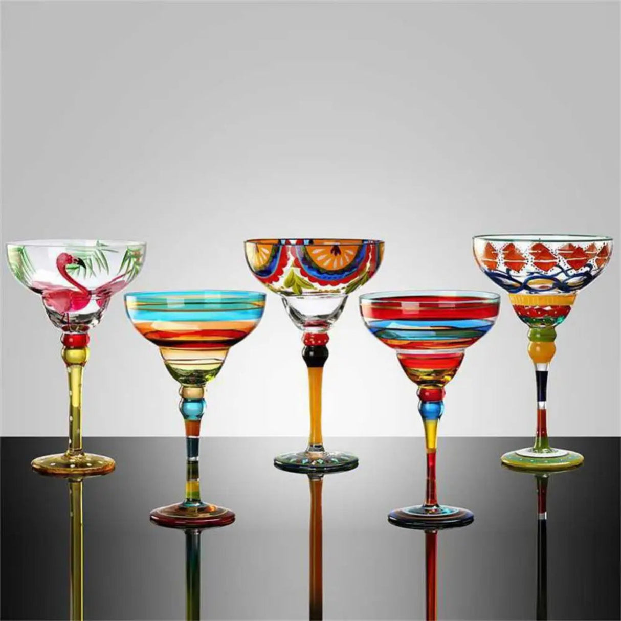 Set of colorful glass cocktail glasses on a reflective surface with a gray background