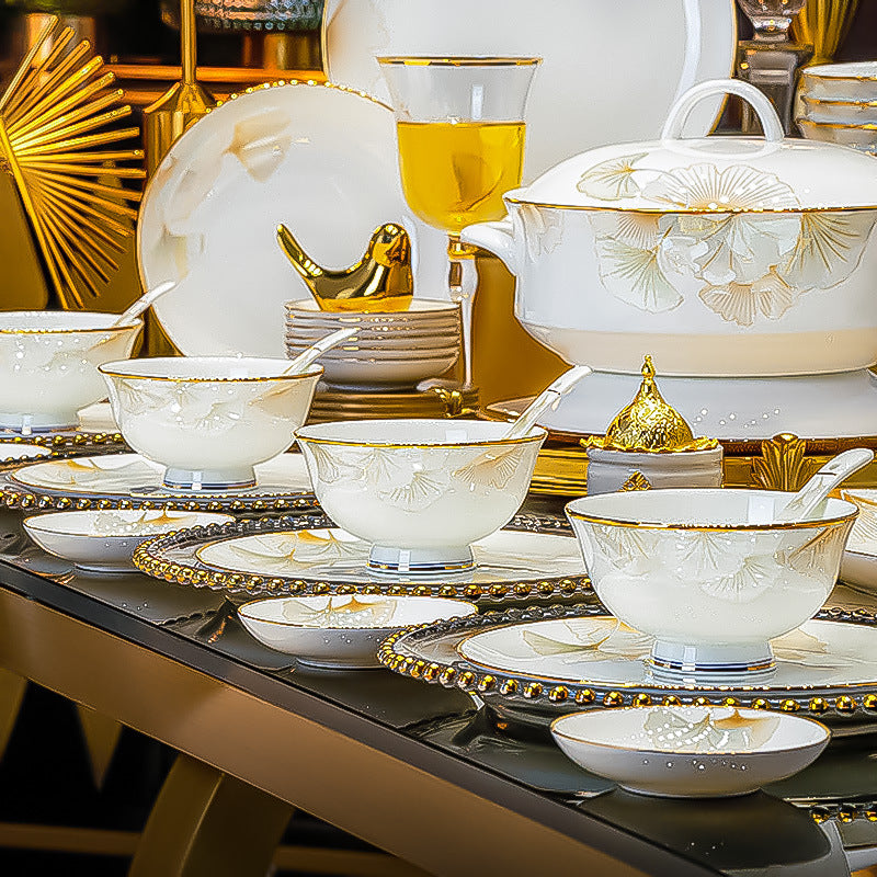 Set of white ceramic tableware with gold accents on a decorative table.