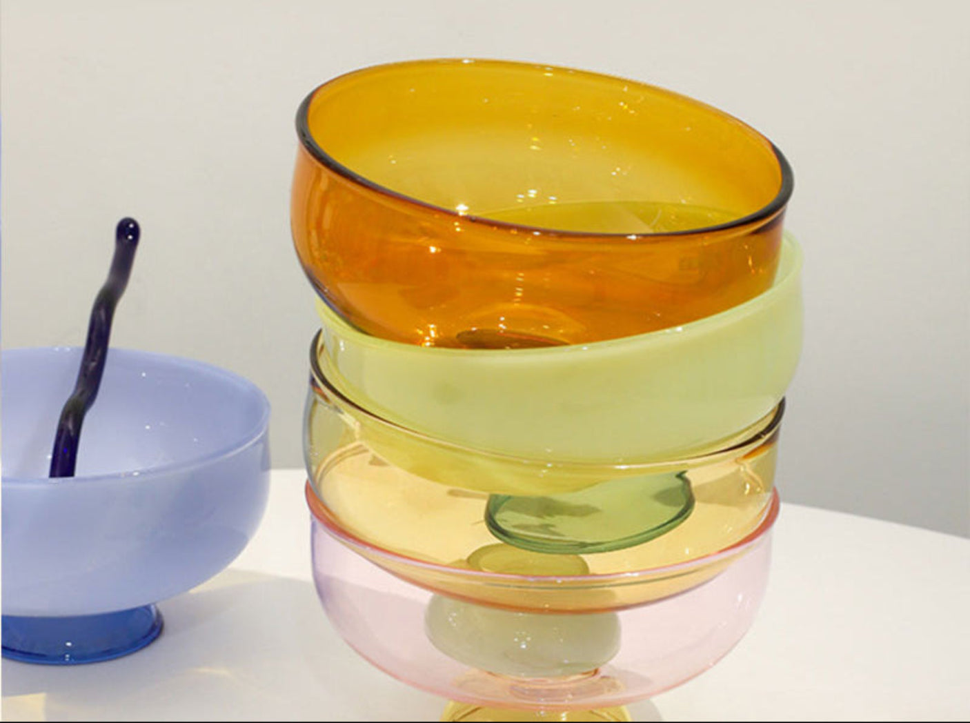 Stack of colorful glass bowls on a white surface with a white background