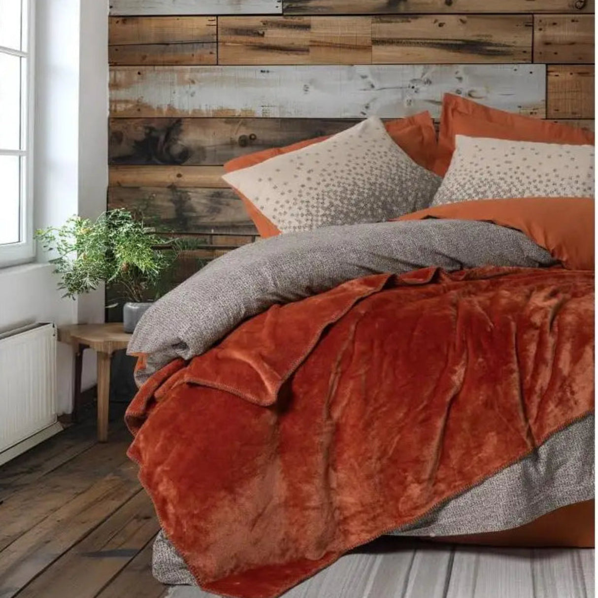Bed with orange bedding and gray pillows against a wooden wall.