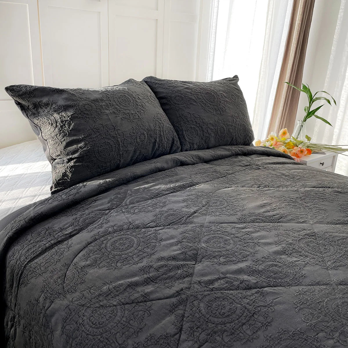 Gray textured comforter set on a bed with pillows in a bright room.