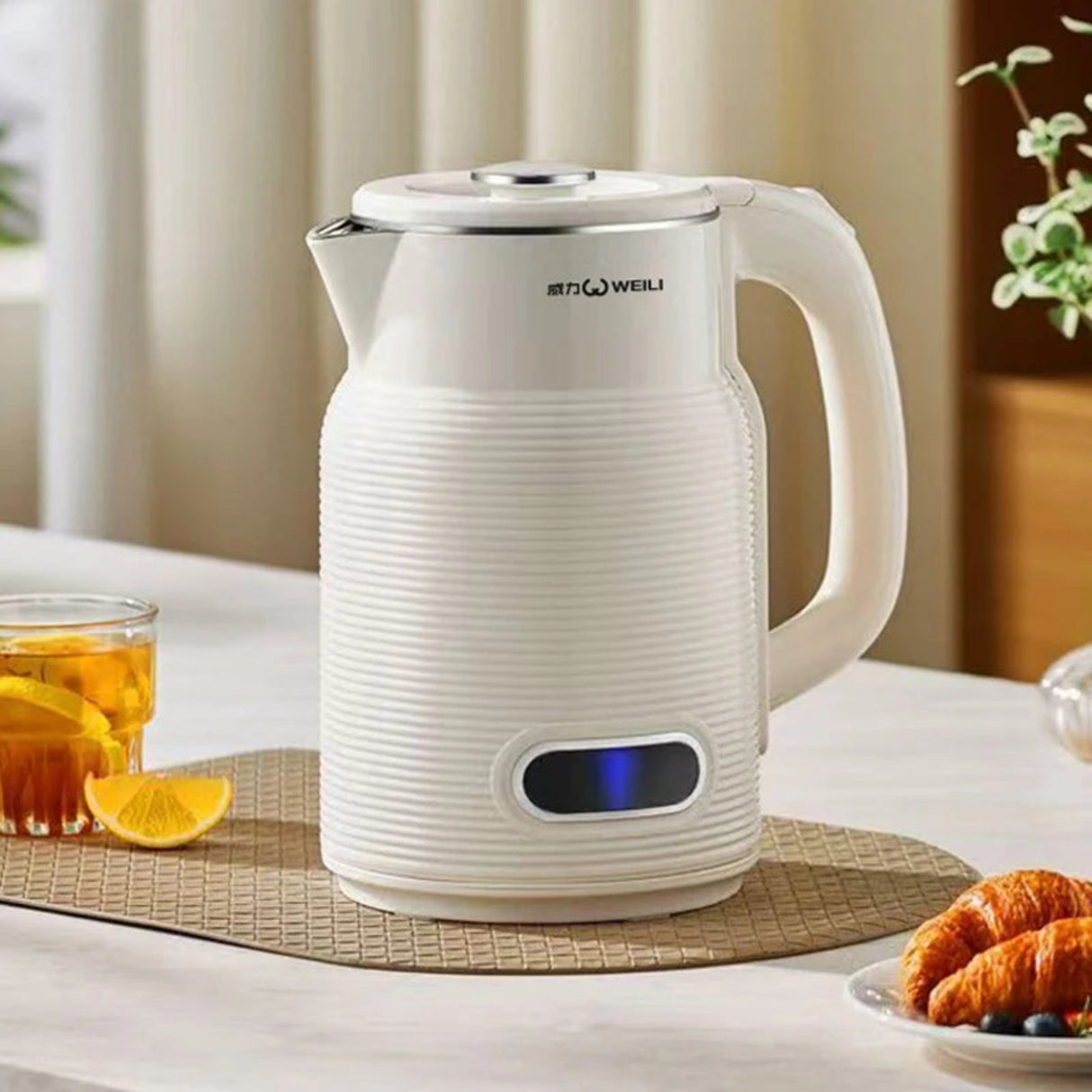 White electric kettle on a table with a glass of tea and croissants in the background