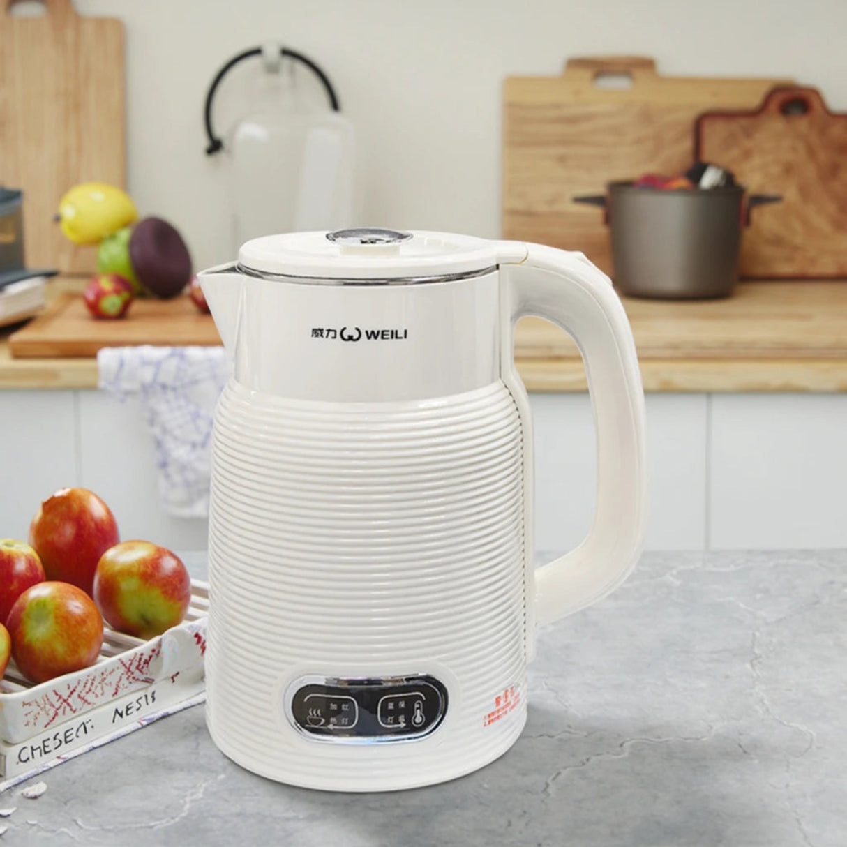 White electric kettle on a kitchen counter with fruits and kitchen utensils in the background