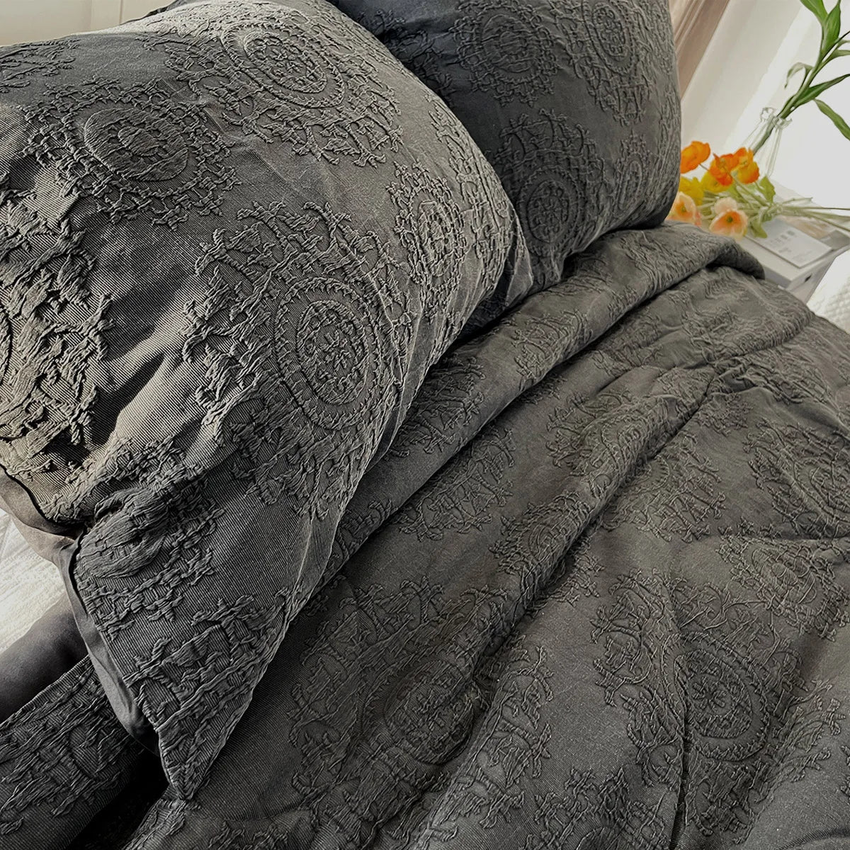 Gray textured comforter and pillows on a bed with a blurred background