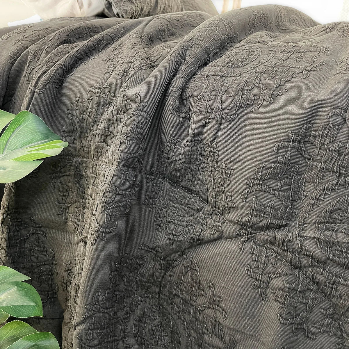 Textured gray blanket with a subtle pattern draped over a surface, with green leaves in the foreground.