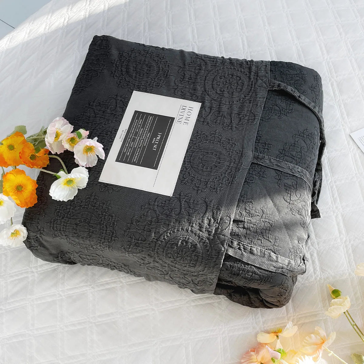 Folded black textured blanket with a label on a white surface with flowers.