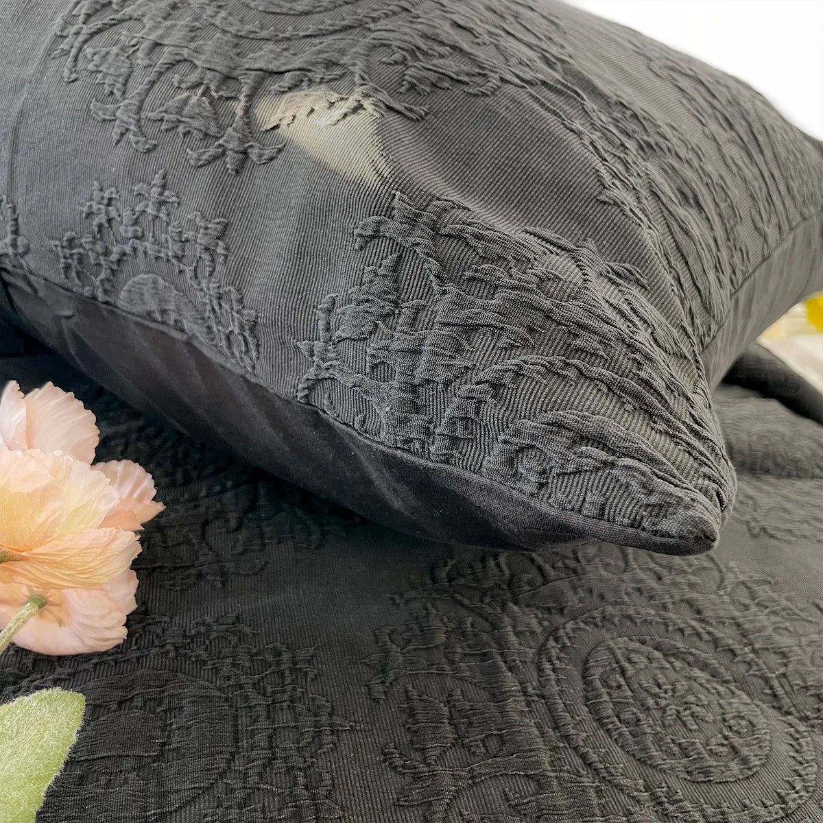 Textured gray pillow and quilt with floral design on a white background