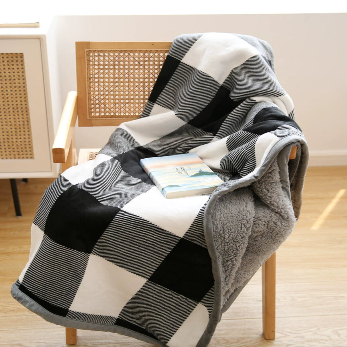 Checkered blanket draped over a chair with a book on a wooden floor.