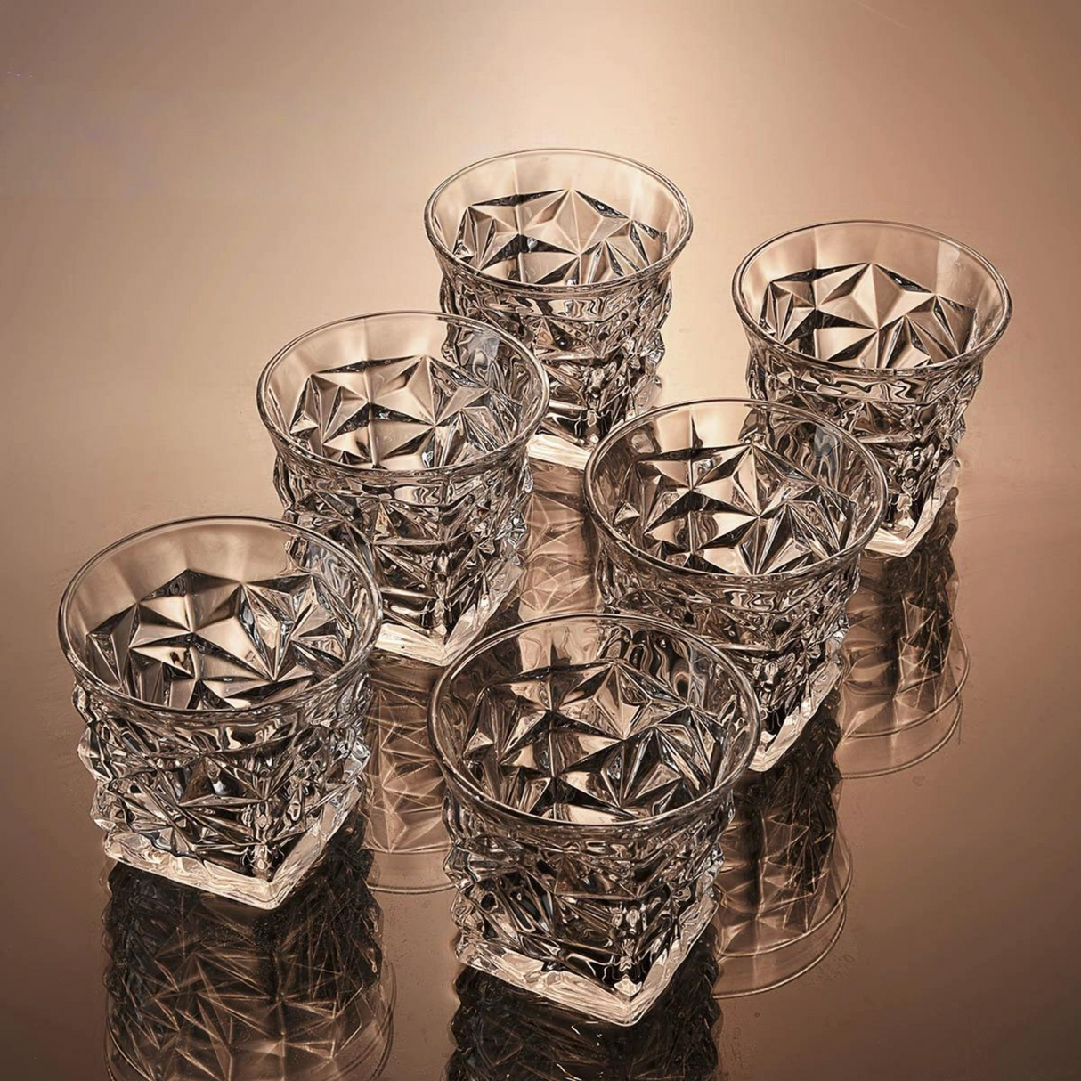 Set of six crystal glasses with diamond cut design on a reflective surface.