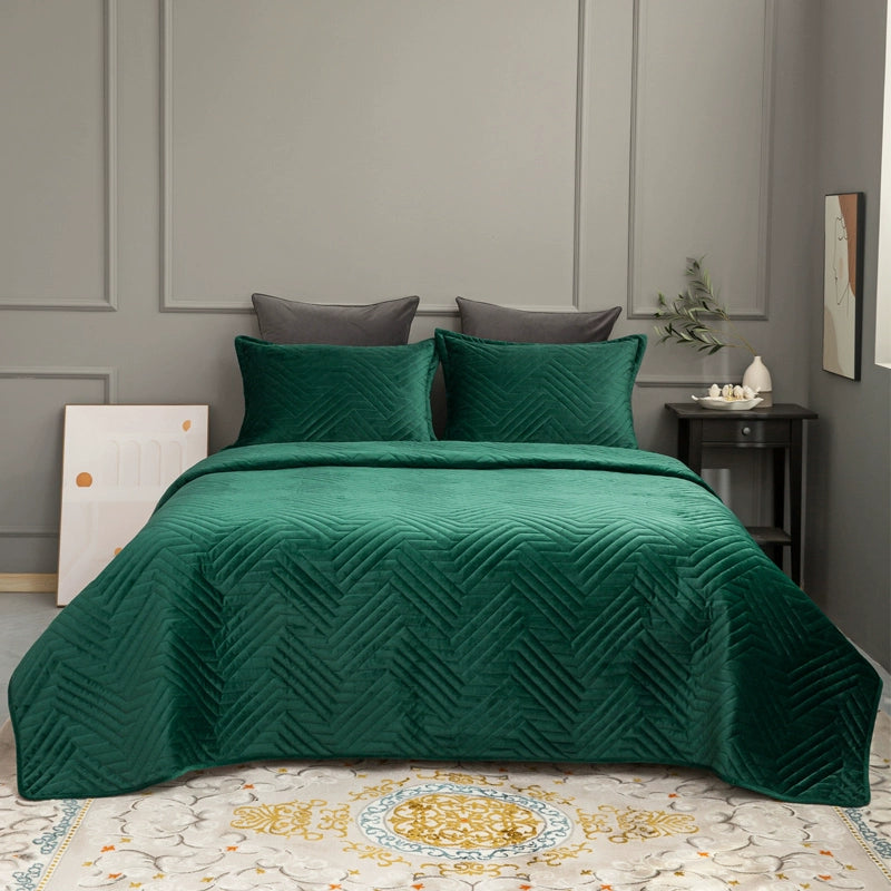 Green quilted coverlet on a bed with gray pillows against a gray paneled wall.