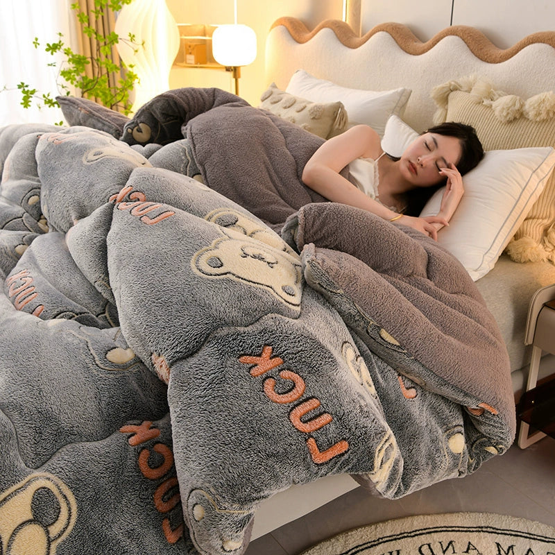 Woman lying on a bed under a gray plush blanket with cartoon designs, in a cozy bedroom setting.