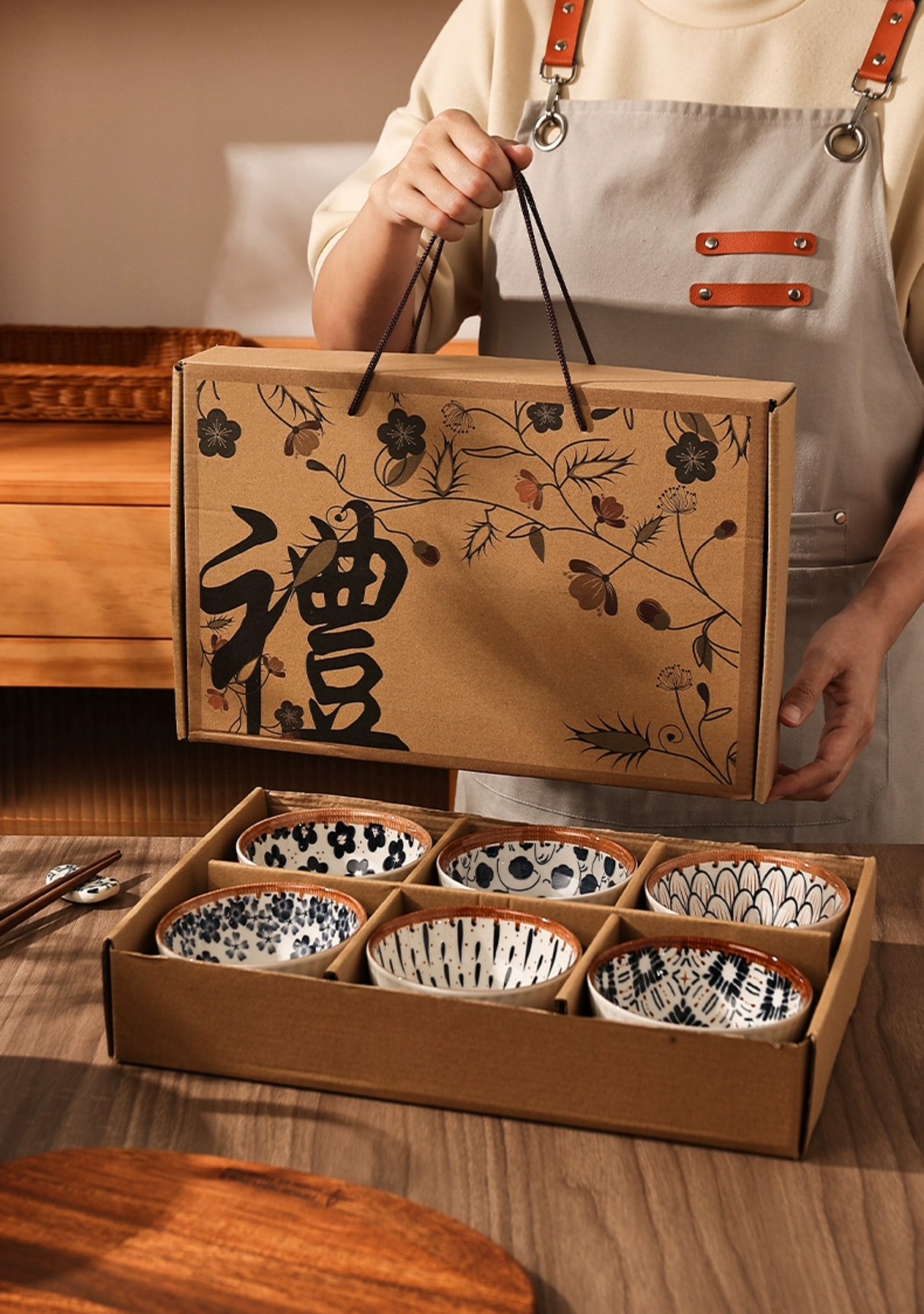 Person holding a box with six small bowls inside, set against a wooden table.