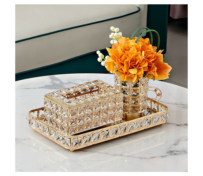 Decorative tray with crystal accents holding a vase of orange flowers on a marble surface.