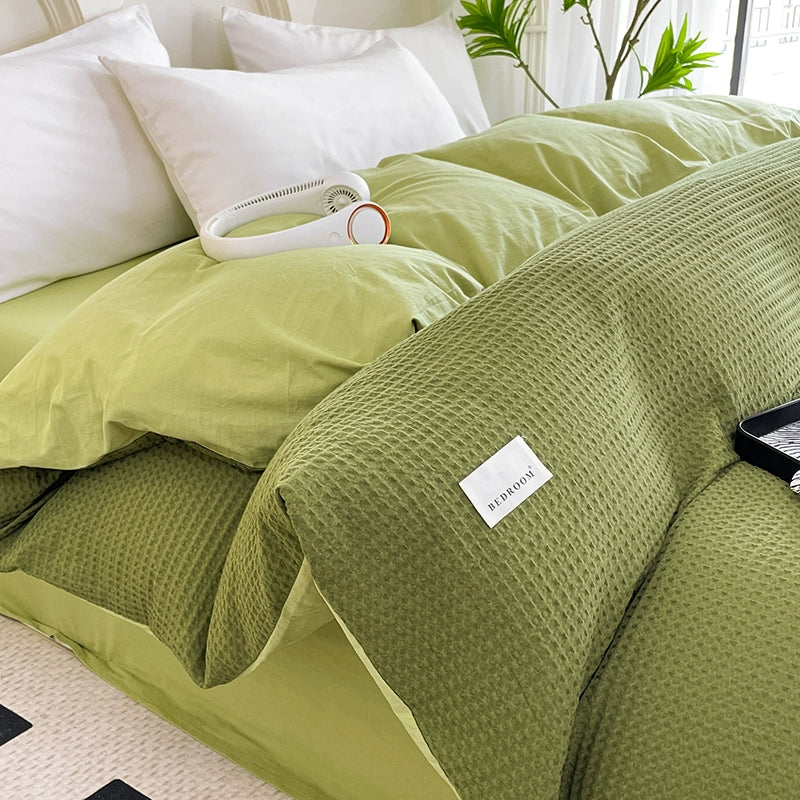 Green textured blanket with a brand label on a bed in a bright room.