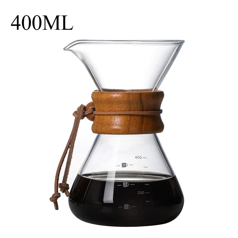 Clear glass coffee maker with wooden collar and brown rope, filled with coffee, on a white background.