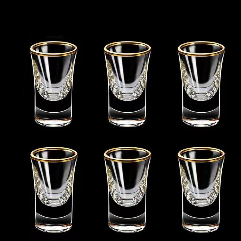 Set of six clear shot glasses with gold rims on a black background