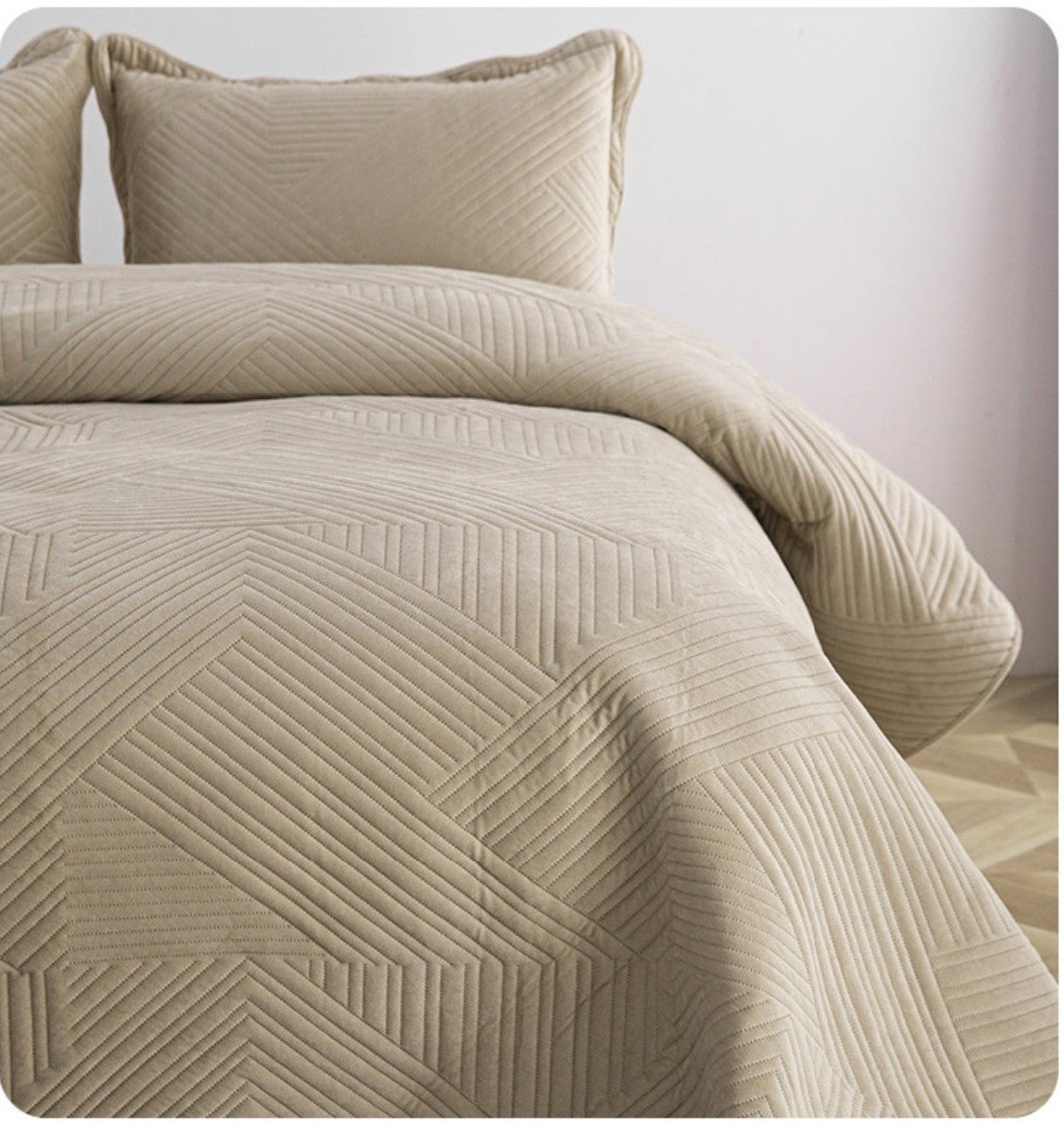 Beige quilt draped over a bed with pillows on a white background