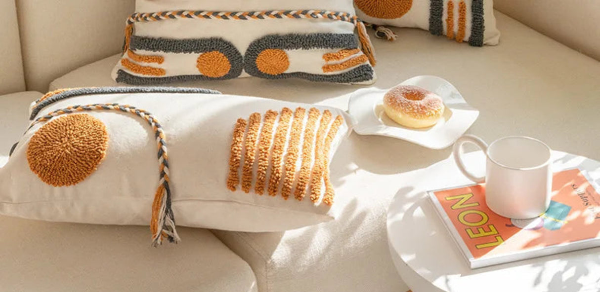 Decorative pillows on a sofa with a cup, book, and donut on a table.