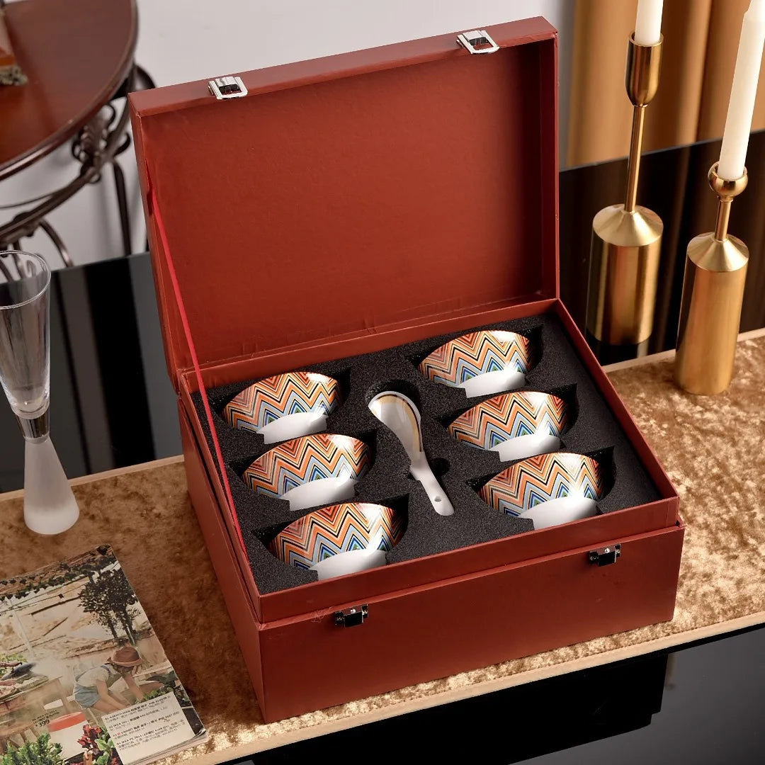 Set of ceramic tea cups with a decorative interior in a red box on a table.