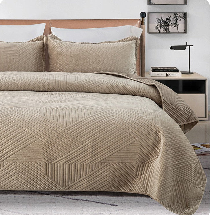 Beige quilted cover on a bed with a nightstand and lamp in a bedroom setting.