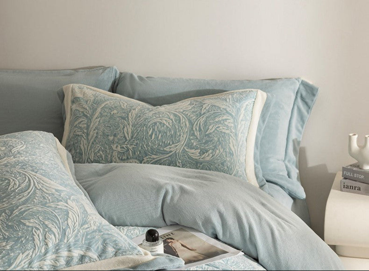 Light blue bedding set with decorative pillows on a bed against a beige wall.