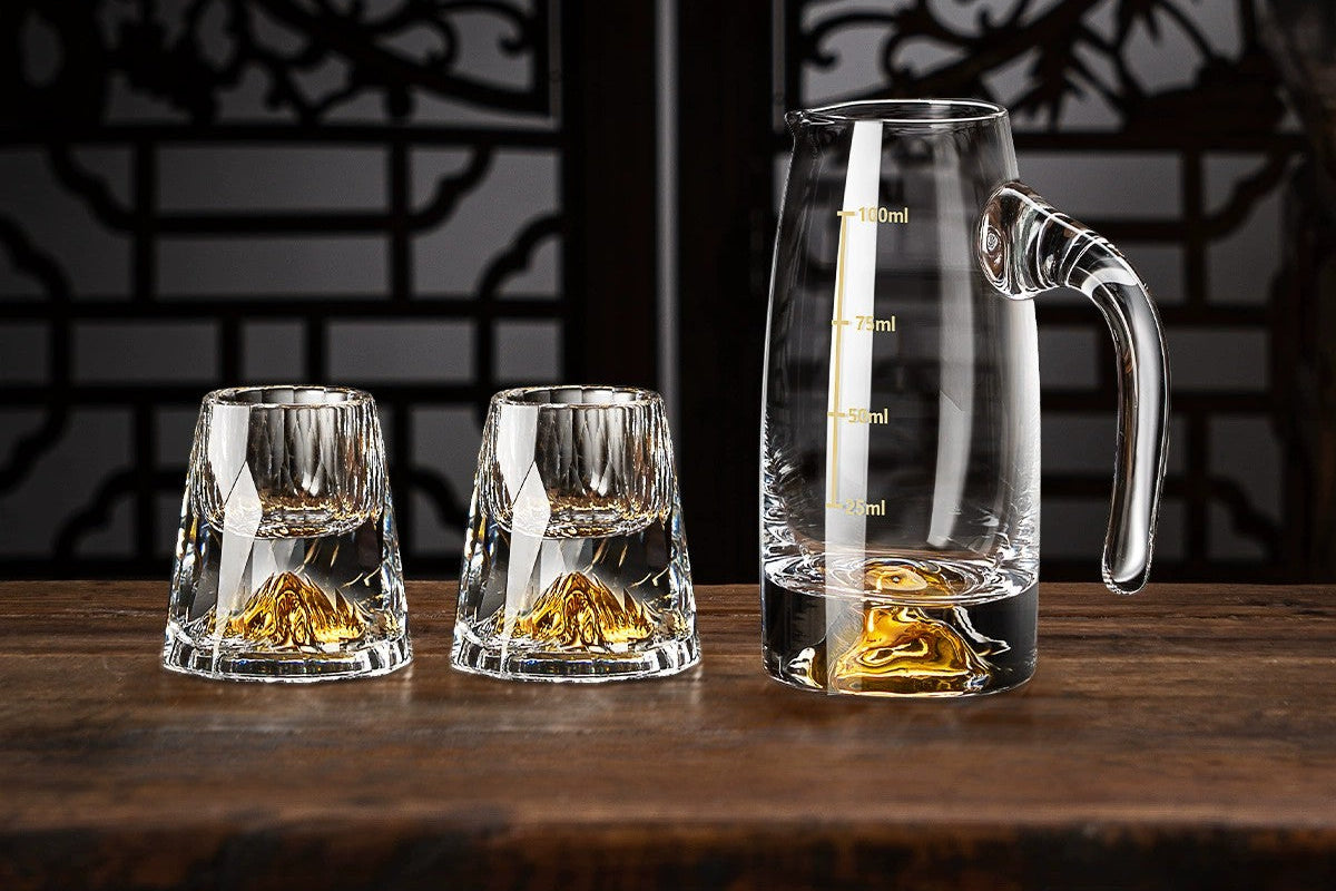 Set of clear glassware with gold accents on a wooden surface against a dark decorative wall.