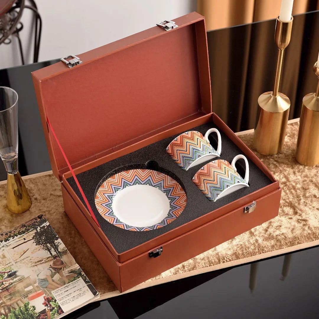 Set of colorful ceramic cups and saucer in a brown leather case on a decorative surface.