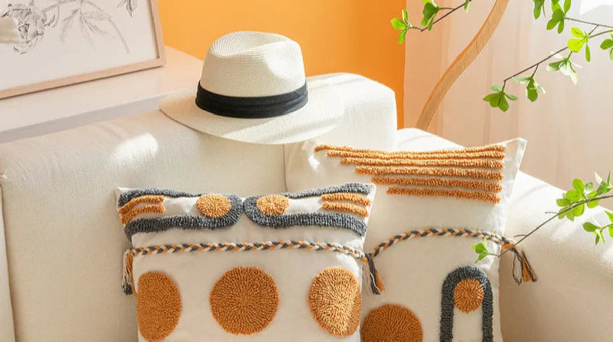 Decorative pillows and a hat on a couch with a warm-toned wall and plant in the background.