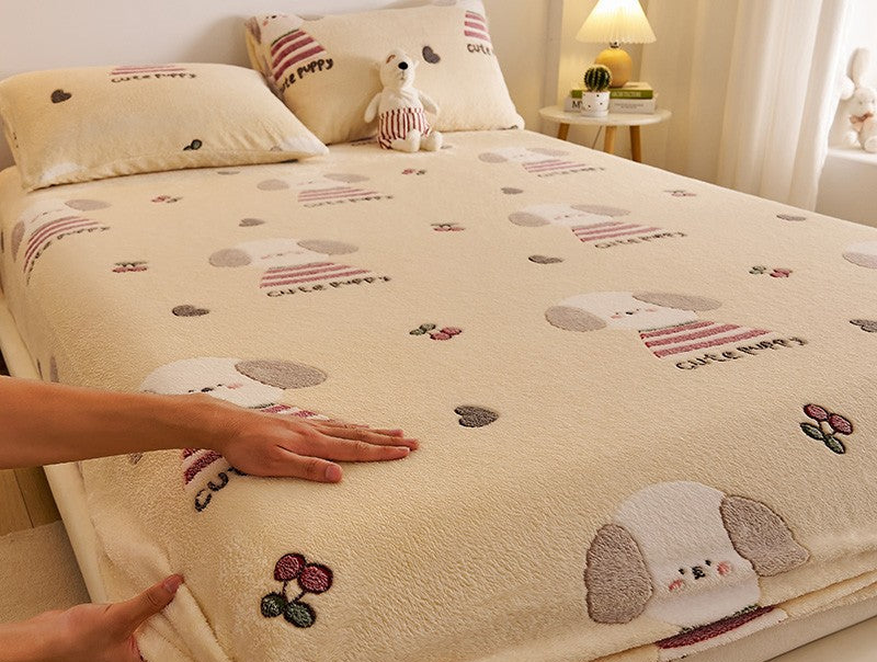 Beige bedspread with cartoon dog design on a bed, with a hand touching it.