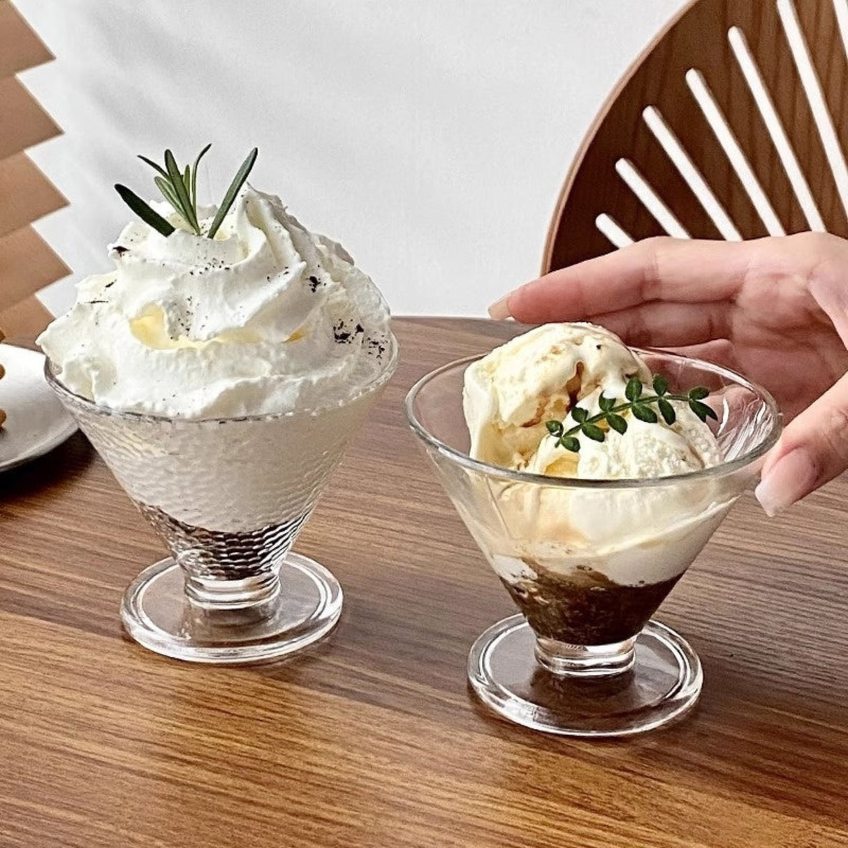 Two dessert glasses with ice cream and whipped cream on a wooden table.