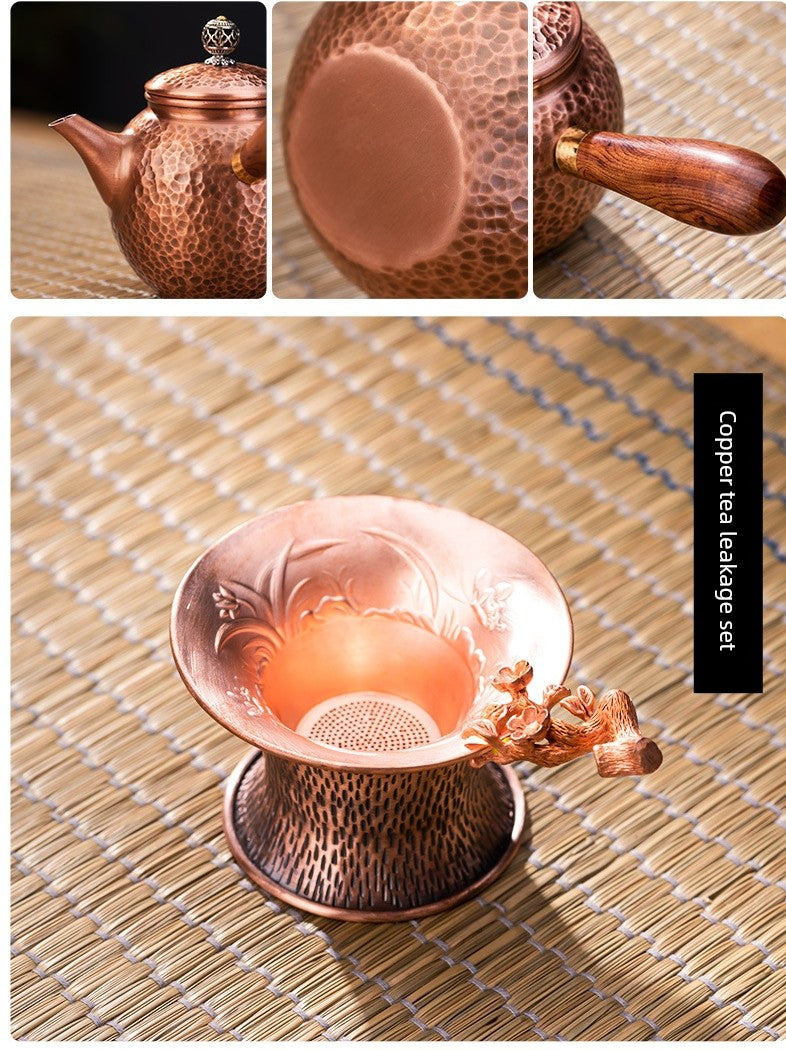 Copper tea set with teapot, cup, and infuser on a woven mat.
