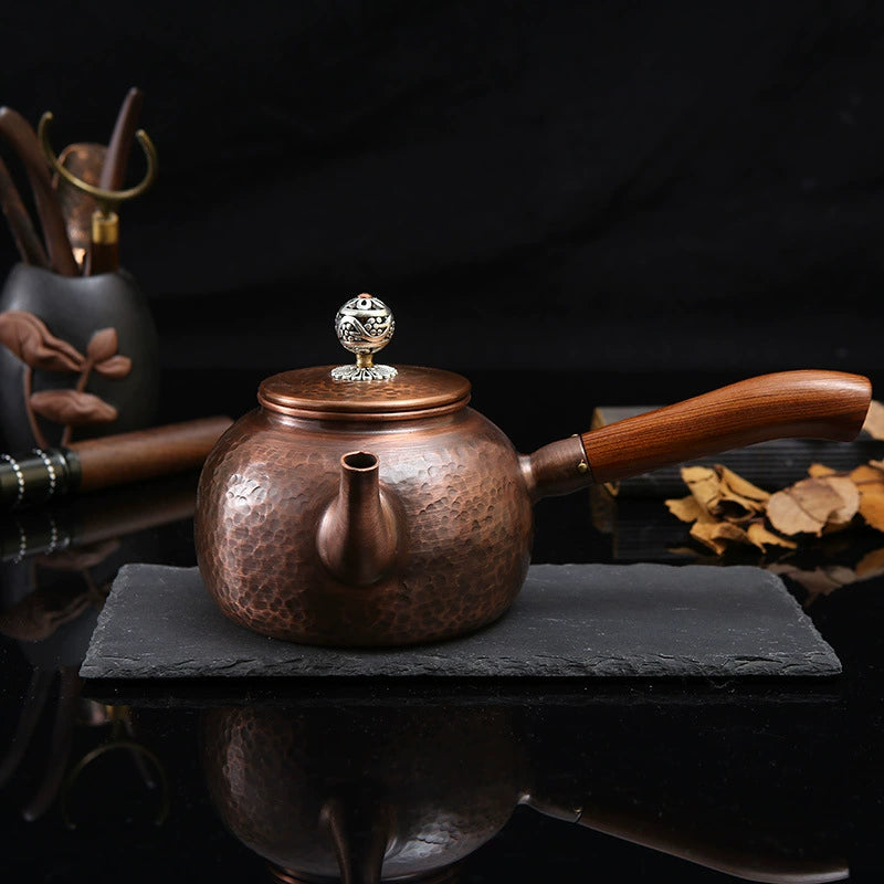 Copper teapot with wooden handle on a dark surface