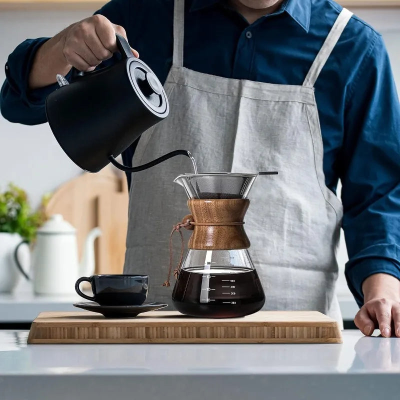 Person pouring coffee from a kettle into a wooden coffee dripper on a kitchen counter.