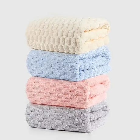 Stack of four textured bath towels in beige, blue, pink, and gray on a light gray background.