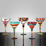 Set of colorful glass cocktail glasses on a reflective surface with a gray background