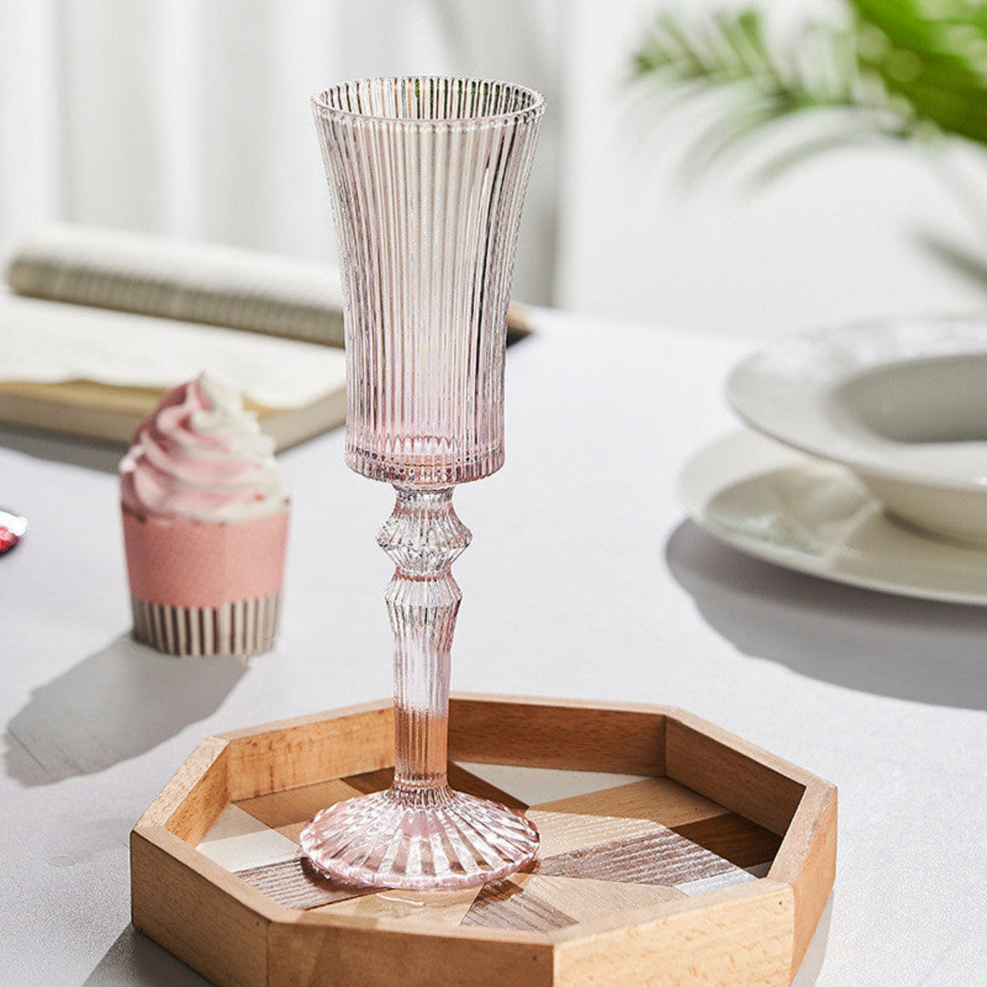 Pink glass candle holder on a wooden tray with a blurred background