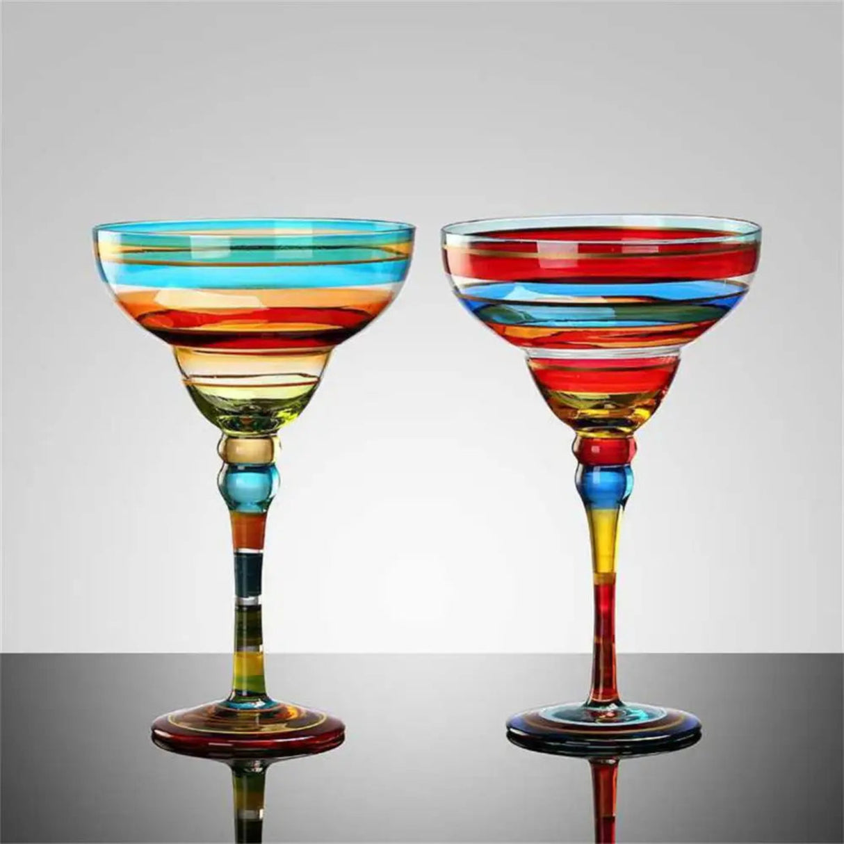 Two colorful striped cocktail glasses on a reflective surface with a gray background
