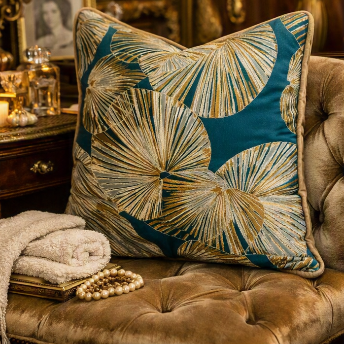 A split-screen lifestyle image showing a decorative throw pillow with a teal and beige palm leaf pattern styled on a tufted sofa in a warm, elegant living room setting.
