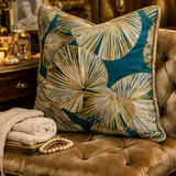 A split-screen lifestyle image showing a decorative throw pillow with a teal and beige palm leaf pattern styled on a tufted sofa in a warm, elegant living room setting.