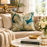 A split-screen lifestyle image showing a decorative throw pillow with a teal and beige palm leaf pattern styled on a tufted sofa in a warm, elegant living room setting.