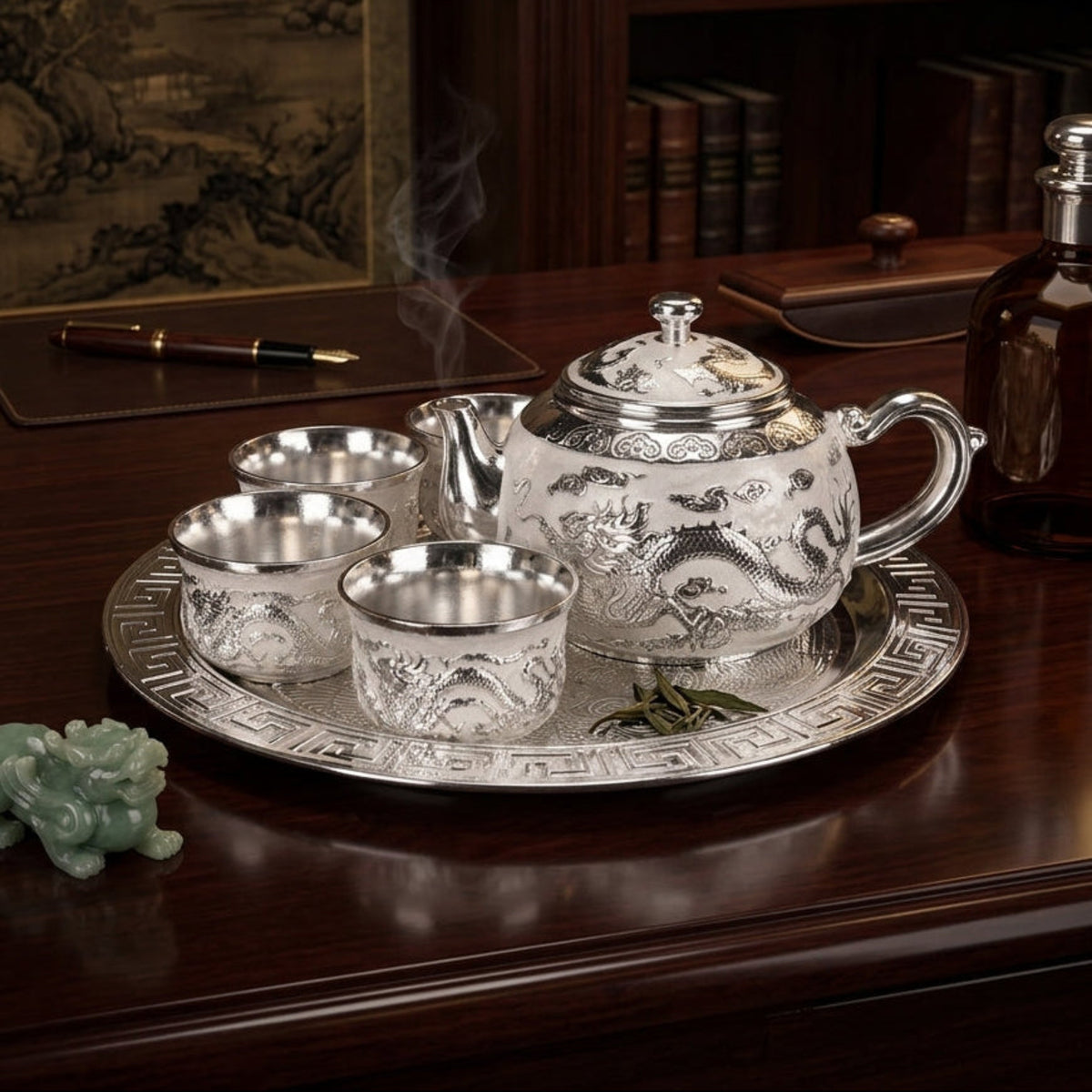 A silver teapot and four matching teacups with dragon engravings, set on a round silver tray on a dark wooden table. Steam rises from the teapot, and a small green jade figurine sits nearby.