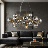 A modern chandelier with multiple reflective silver glass globes and warm gold-toned metal accents hangs above a dark gray sectional sofa in a contemporary living room.