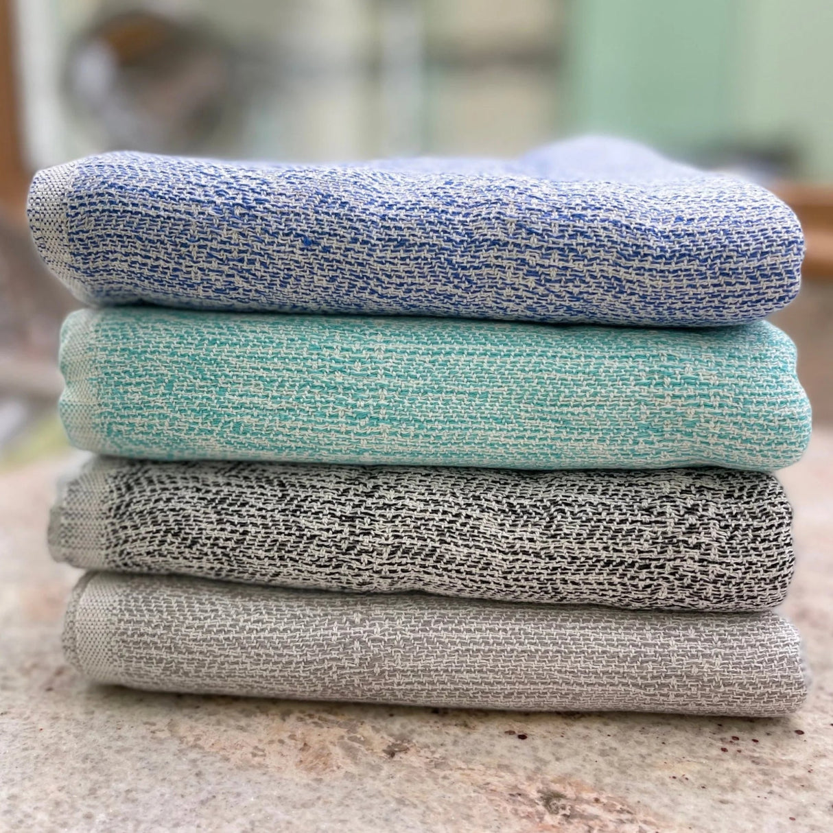 Stack of three textured cloths in blue, green, and gray on a marble surface.
