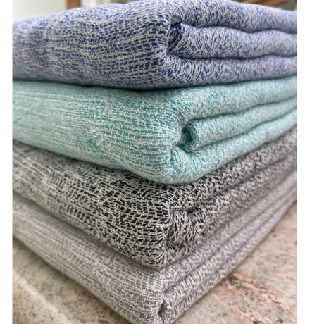 Stack of folded textured towels in blue, green, and gray on a marble surface.