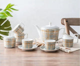 Tea set with plaid design on a wooden table with a plant in the background