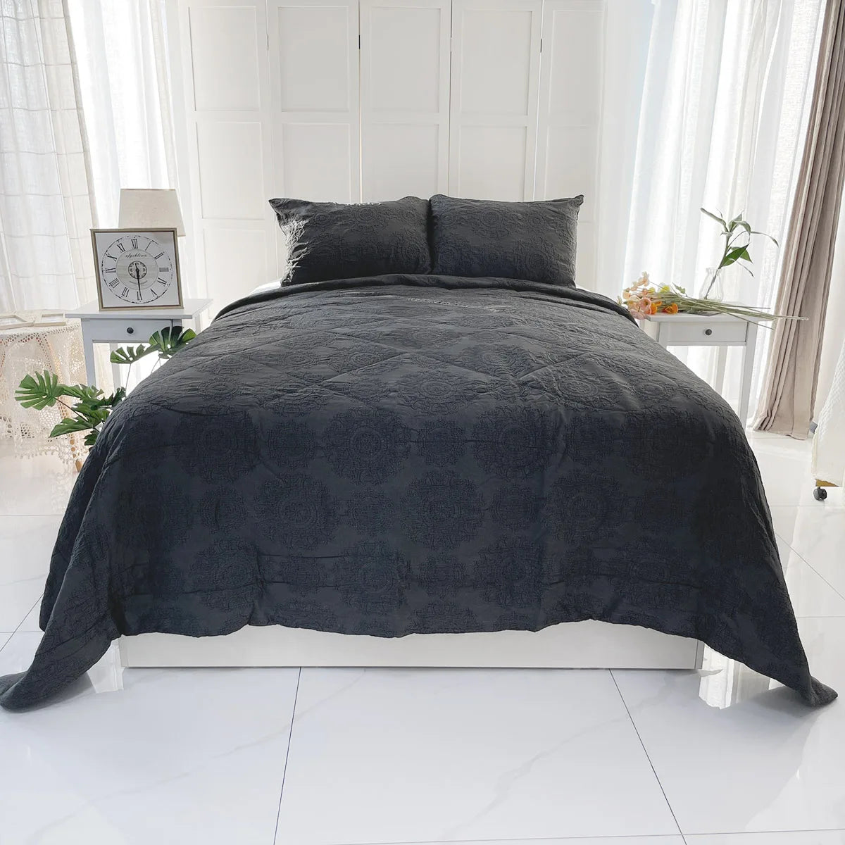 Dark gray quilted comforter set on a bed in a bright room with white walls and light-colored floor.