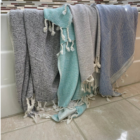 Three towels with tassels hanging on a towel rack against a tiled wall.