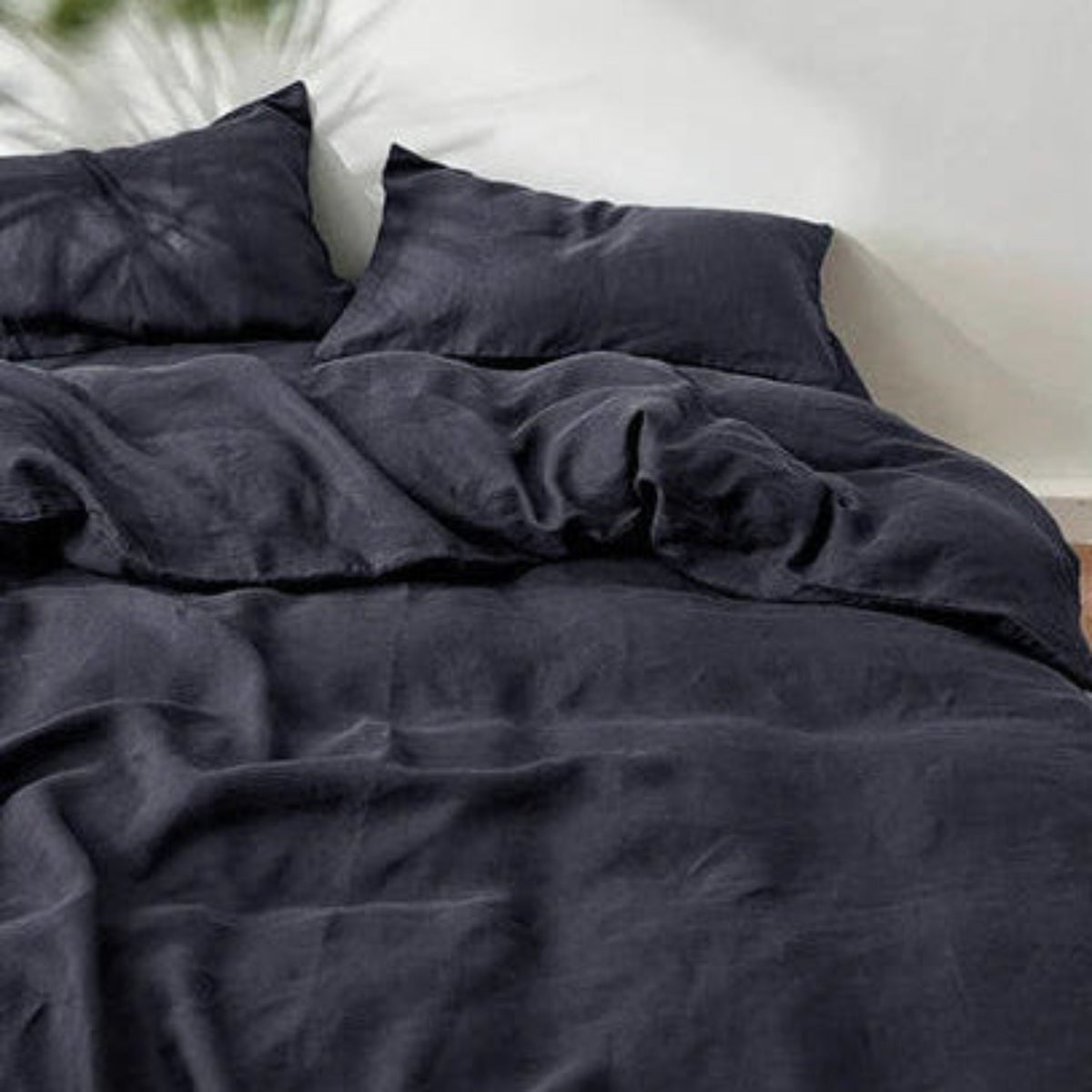 A collage showing a dark charcoal gray bedding set in multiple views: a made bed, folded sheets, and a rolled bedding corner on a bed. The bedding appears soft and slightly textured, with matching pillowcases.