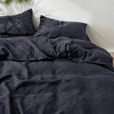 A collage showing a dark charcoal gray bedding set in multiple views: a made bed, folded sheets, and a rolled bedding corner on a bed. The bedding appears soft and slightly textured, with matching pillowcases.
