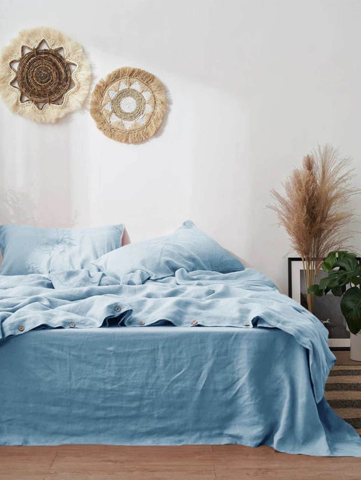Two bedroom scenes showing bedding in different colorways: a top view with light blue sheets and pillows, and a bottom view with gray sheets and pillows, both styled with wall decor, pampas grass, and plants.